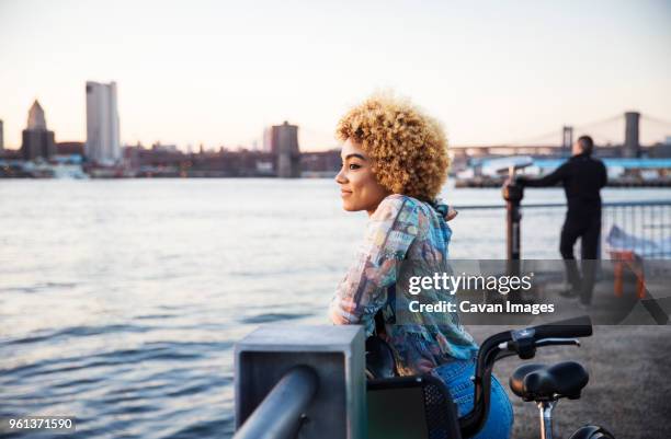 thoughtful woman relaxing at railing by river in city - black woman riding bike stock pictures, royalty-free photos & images