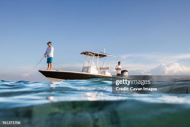 low angle view of men fishing while standing on boat at sea against sky - fischen stock-fotos und bilder