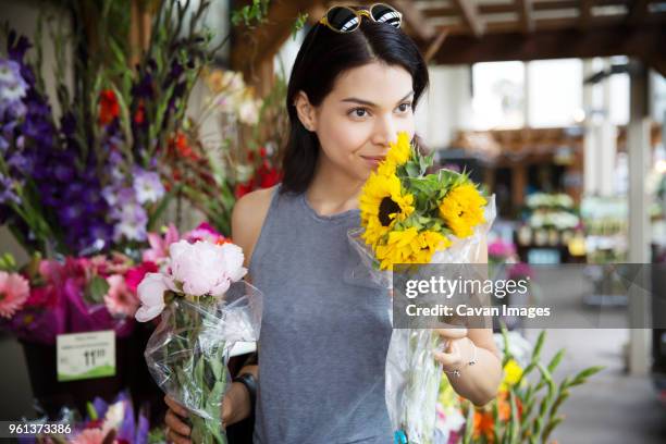 beautiful woman smelling sunflowers at flower shop - flower shop stockfoto's en -beelden