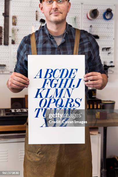 male craftsperson holding poster and standing in printing press - affiche spectacle stockfoto's en -beelden