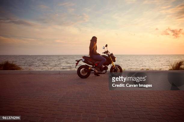 side view of woman riding motorcycle on street against sea during sunset - mare moto foto e immagini stock