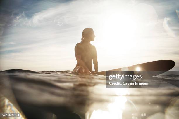 surface level of woman sitting on surfboard in sea during summer - woman surfing stock pictures, royalty-free photos & images