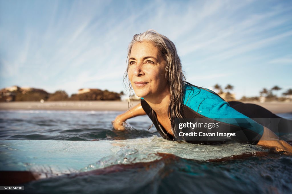 Mature woman looking away while surfing on sea