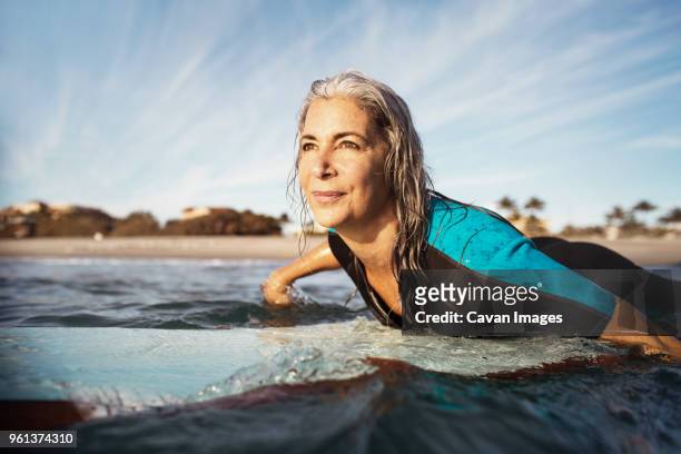 mature woman looking away while surfing on sea - peace & sports stock pictures, royalty-free photos & images