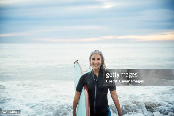 portrait of happy wet female surfer carrying surfboard at delray beach - beach hold surfboard stock-fotos und bilder