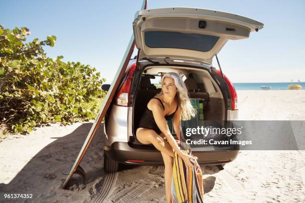 female surfer wiping legs while sitting in car trunk at delray beach - delray beach open stockfoto's en -beelden