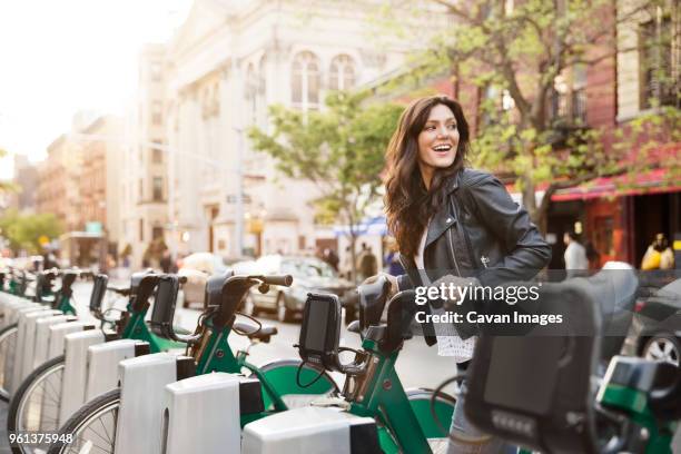 happy woman unlocking bike share on street - bicycle rental stock-fotos und bilder