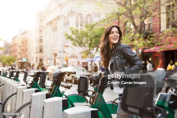 happy woman unlocking bike share on street - bicycle rental stockfoto's en -beelden