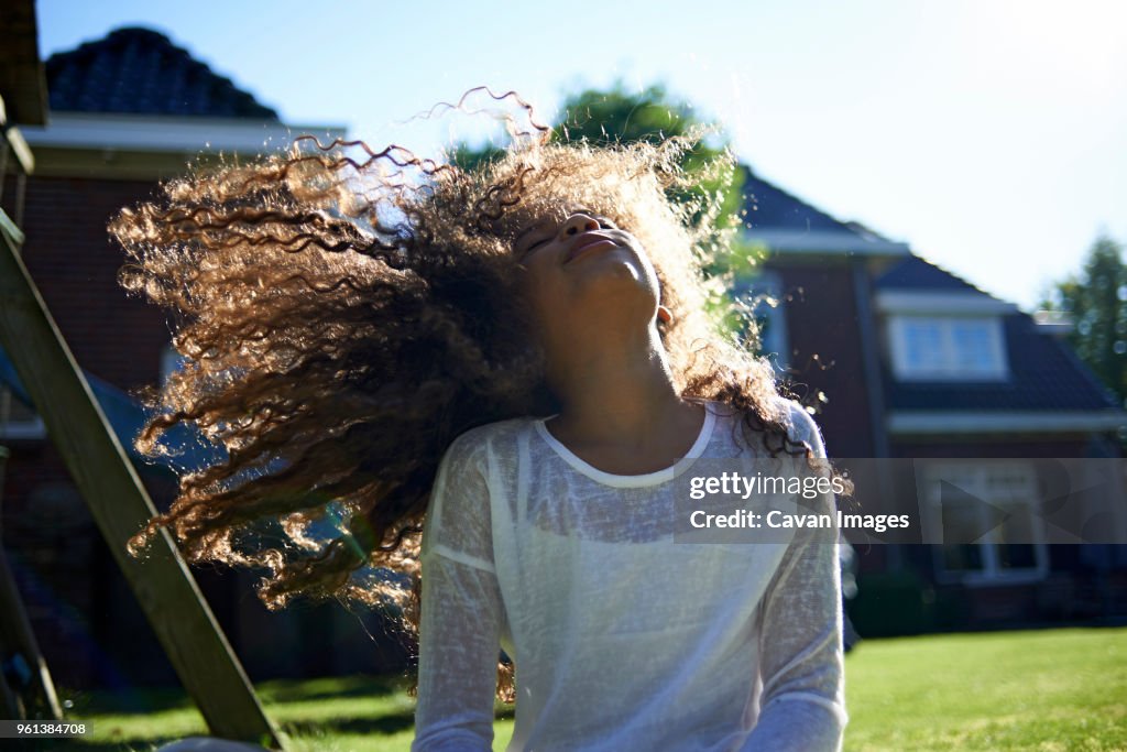 Happy girl shaking head while standing against house in backyard