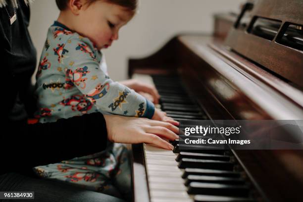 son sitting with mother playing piano at home - musikalische begleitung stock-fotos und bilder