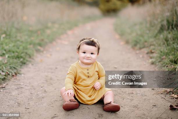 portrait of cute baby girl sitting on dirt road - weibliches baby stock-fotos und bilder