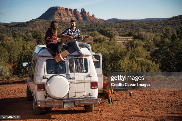 man playing guitar while sitting with friend on car roof - southwest music stock pictures, royalty-free photos & images