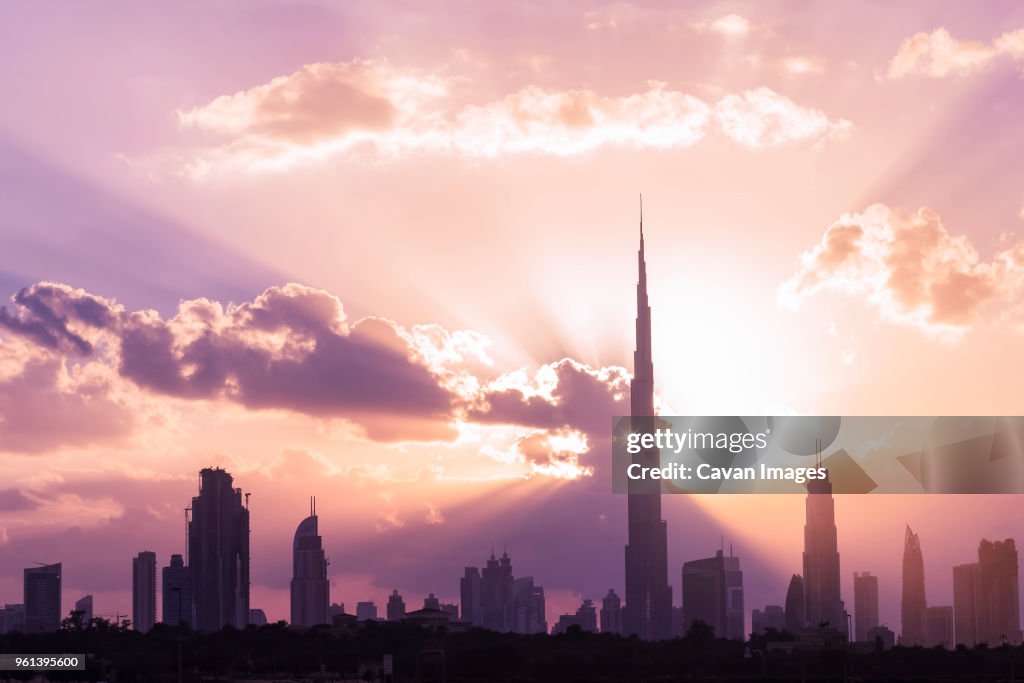 Silhouette Burj Khalifa and skyscrapers against cloudy sky during sunset