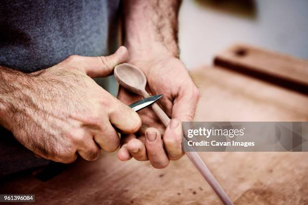 midsection of carpenter carving wooden spoon with knife in workshop - wooden spoon stock pictures, royalty-free photos & images
