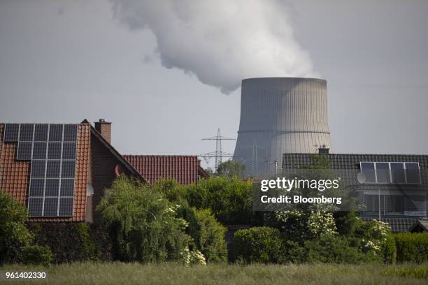 Solar panels sit on the roofs of residential property as a cooling tower emits vapor beyond at the coal powered power plant operated by RWE AG in...