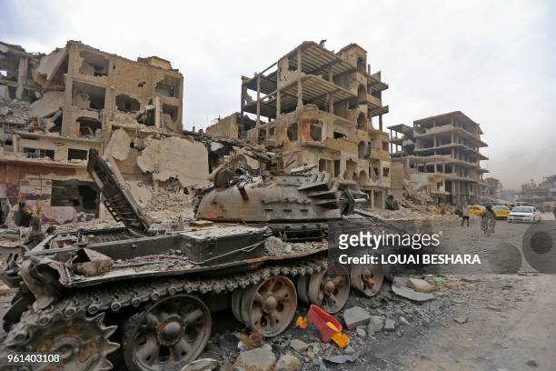 Picture taken on May 22, 2018 shows a destroyed tank in front of damaged buildings in the Hajar al-Aswad neighbourhood on the southern outskirts of...