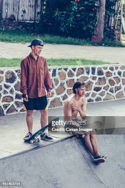 young male friends resting with skateboards at the edge of concrete pool - friends skating stock pictures, royalty-free photos & images