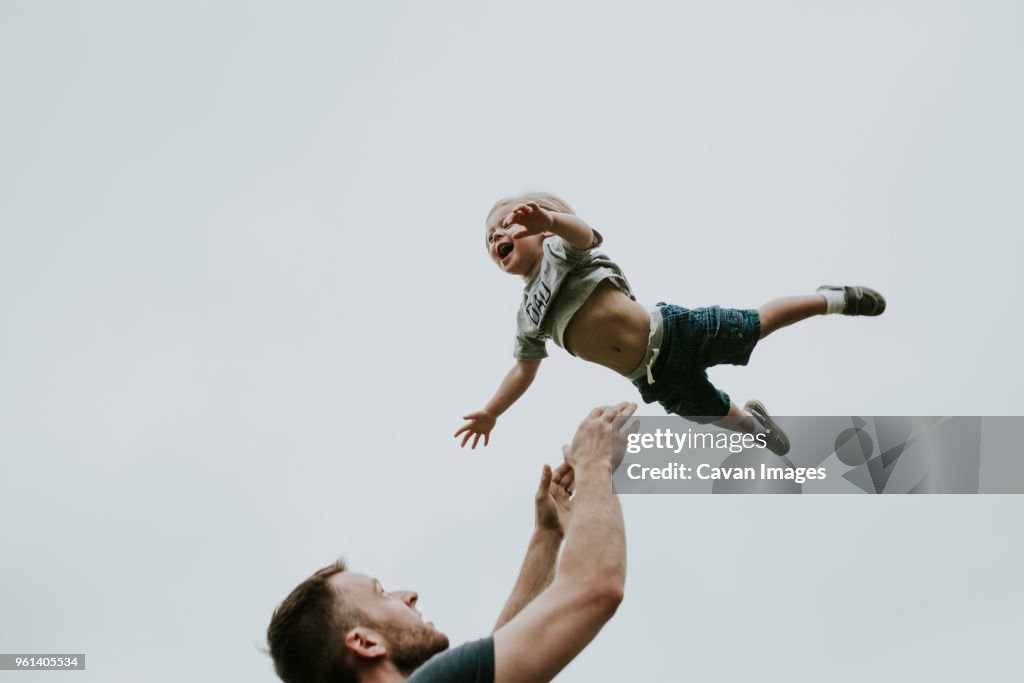 Playful father throwing son in air against clear sky