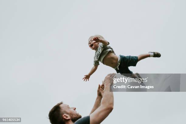 playful father throwing son in air against clear sky - dad throwing kid in air stockfoto's en -beelden