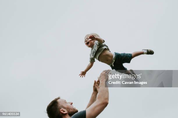 playful father throwing son in air against clear sky - dad throwing kid in air imagens e fotografias de stock