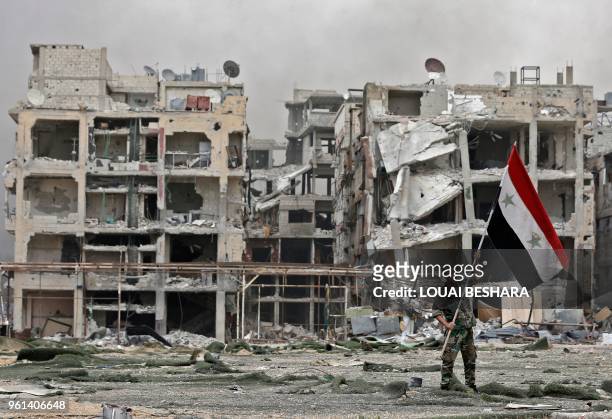 Member of the Syrian pro-government forces carries the national flag as he stands in front of damaged buildings in the Yarmuk Palestinian refugee...