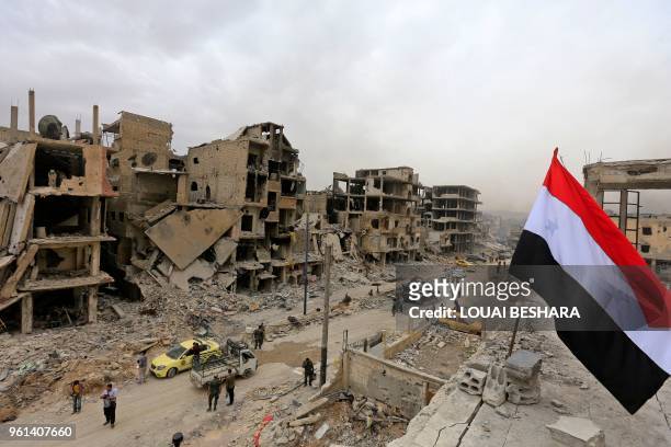 Picture taken on May 22, 2018 shows the Syrian national flag atop a building in a devastated street in the Hajar al-Aswad neighbourhood on the...
