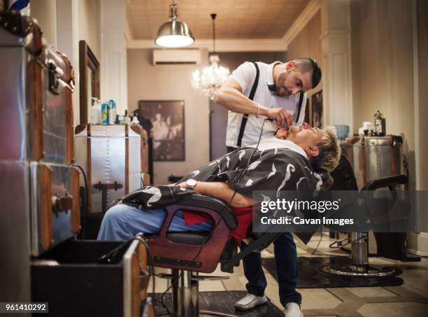 barber shaving man's beard in shop - barber shop stockfoto's en -beelden