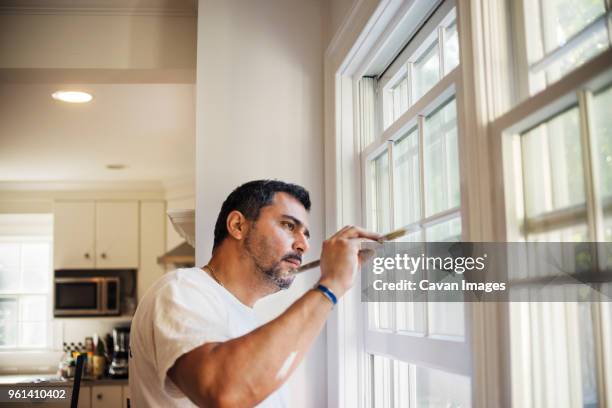 side view of man painting window frame at home - windowframe stock-fotos und bilder