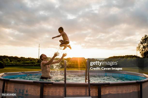 father catching son while swimming in wading pool against cloudy sky at backyard during sunset - planschbecken stock-fotos und bilder