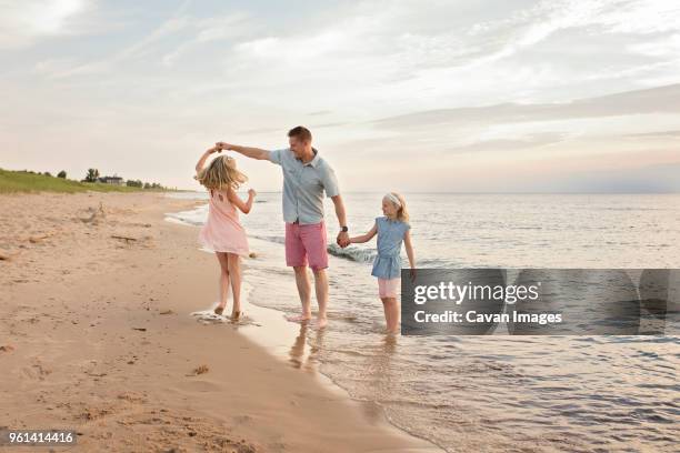 father playing with daughters on shore at beach - three girls at beach stock pictures, royalty-free photos & images