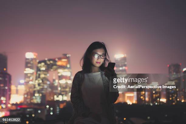 chinese woman using smartphone on skyscraper roof at night - asien metropole nachtleben stock-fotos und bilder