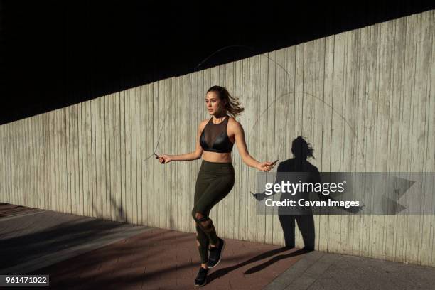 young woman skipping while exercising against wall - jump rope stock pictures, royalty-free photos & images