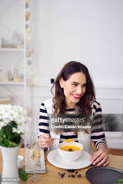 happy woman drinking pumpkin soup while sitting at dinning table - soup home foto e immagini stock