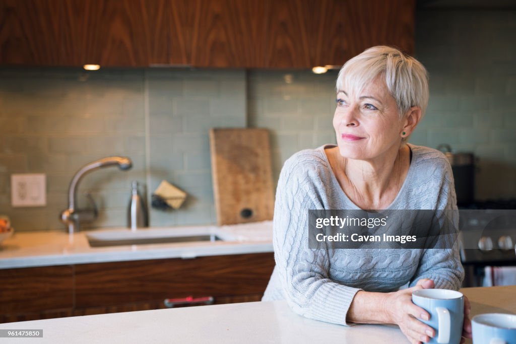 Thoughtful senior woman looking away while leaning on table