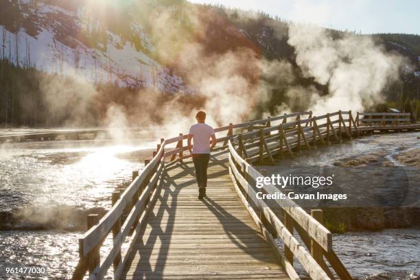 rear view of hiker walking on boardwalk by hot springs at yellowstone national park - mammoth hot springs fotografías e imágenes de stock