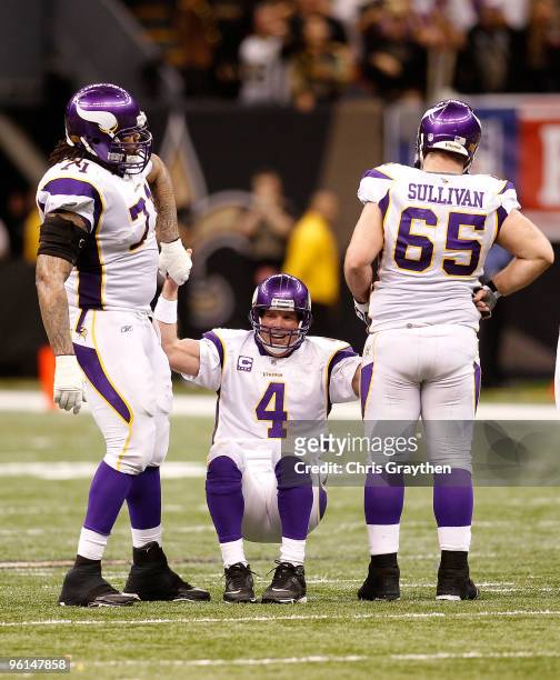 Brett Favre of the Minnesota Vikings is helped up by teammates Phil Loadholt and John Sullivan after he took a hard hit in the second half against...