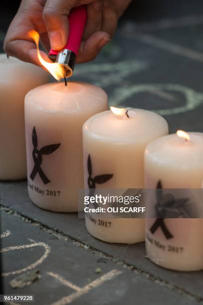 People pay their respects as they light candles bearing Ariana Grande's symbol adjacent to flowers and balloons left in central Manchester on May 22...