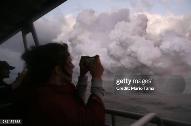 Woman takes photos while riding a tour boat to view Kilauea volcano lava entering the Pacific Ocean at dawn, as a steam plume rises, on Hawaii's Big...