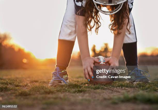 low section of girl holding american football while standing on grassy field against sky during sunset - girl american football player stock pictures, royalty-free photos & images