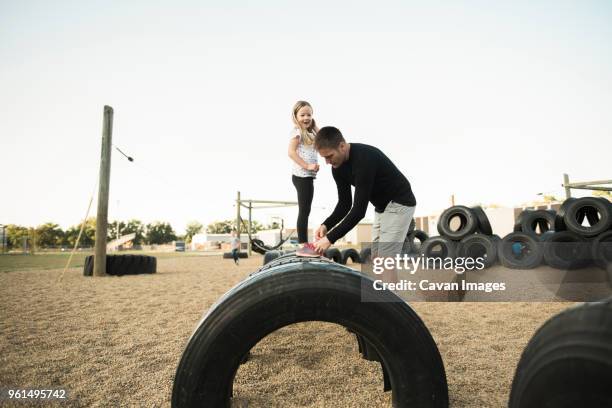 father tying daughter's shoelace standing on tire at playground - shoelace stock pictures, royalty-free photos & images