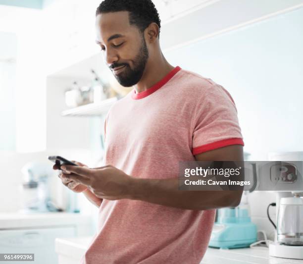 smiling man using phone while standing at kitchen counter - mid adult men stock pictures, royalty-free photos & images