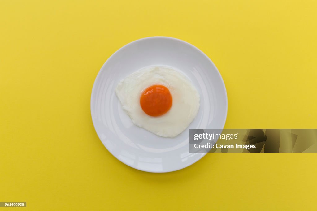 Overhead view of fried egg in plate on yellow background