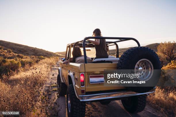 rear view of female friends in off-road vehicle on field against clear sky - 4x4 stock pictures, royalty-free photos & images