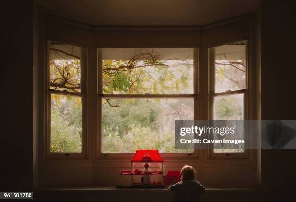 rear view of baby girl playing with dollhouse at bay window in house - janela saliente - fotografias e filmes do acervo