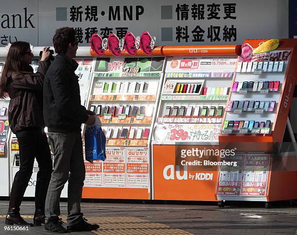 Couple looks at various models of KDDI Corp. Mobile phones displayed outside an electronics store in Tokyo, Japan, on Monday, Jan. 25, 2010. KDDI...