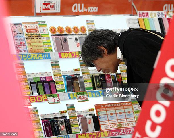 Customer looks at KDDI Corp. Mobile phones displayed at an electronics store in Tokyo, Japan, on Monday, Jan. 25, 2010. KDDI Corp., Japan's...