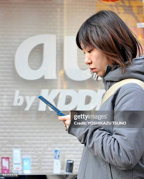 Woman uses her mobile phone before a cellular shop of Japan's telecommunication giant KDDI in Tokyo on January 25, 2010. KDDI's net profit for the...