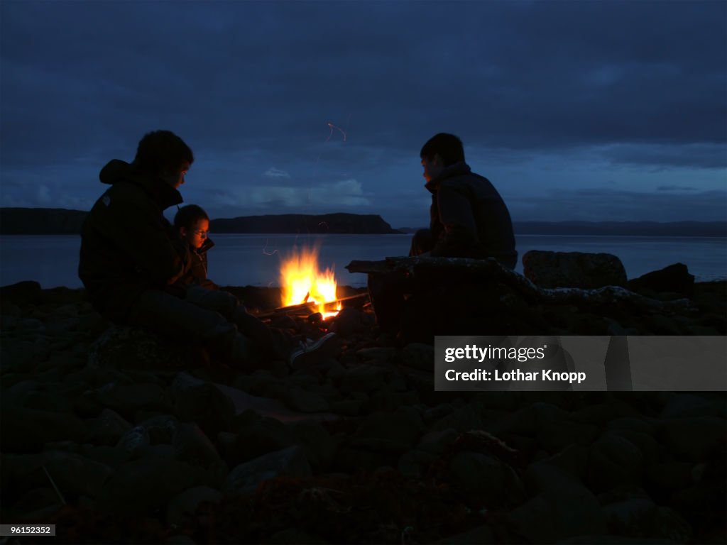 Three boys sitting at campfire