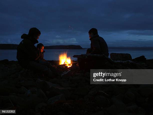 three boys sitting at campfire - bonfire beach stock pictures, royalty-free photos & images