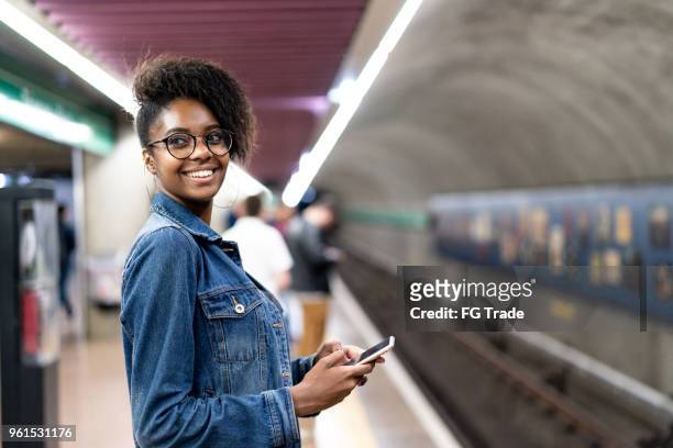 jonge zwarte vrouw met afro kapsel met behulp van mobiele in de metro - mobile apps stockfoto's en -beelden